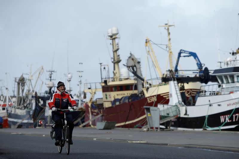 FILE PHOTO: A man rides his bicycle past a row of docked fishing ships in the village of Thyboron in Jutland, Denmark