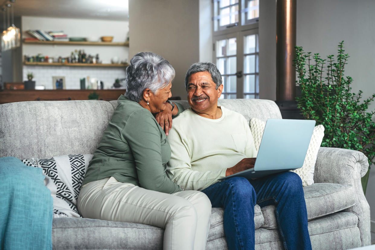 Older couple sitting on the couch; man has laptop open on his lap. 