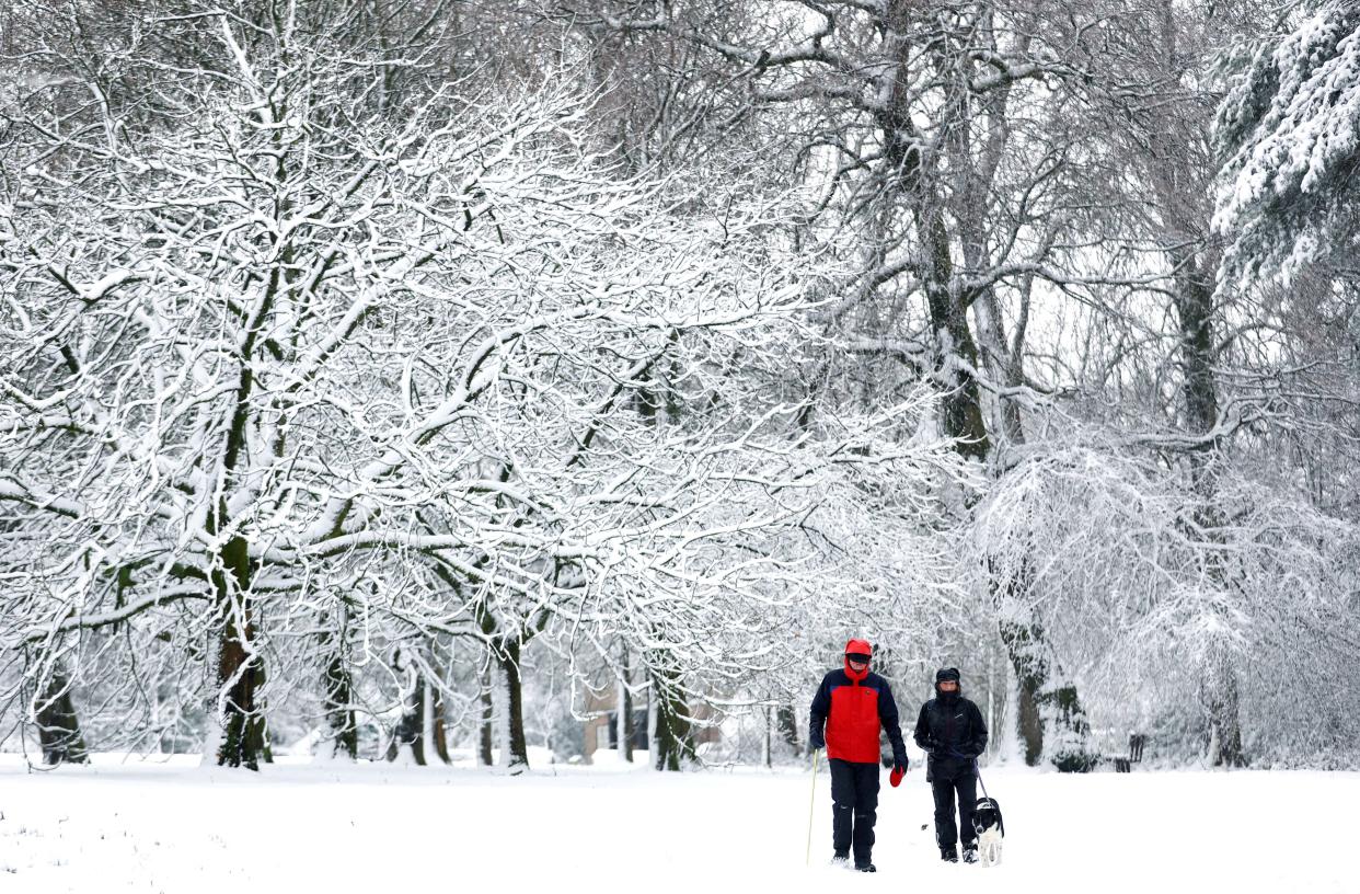 People walk their dog through a snow covered park in Buxton (REUTERS)