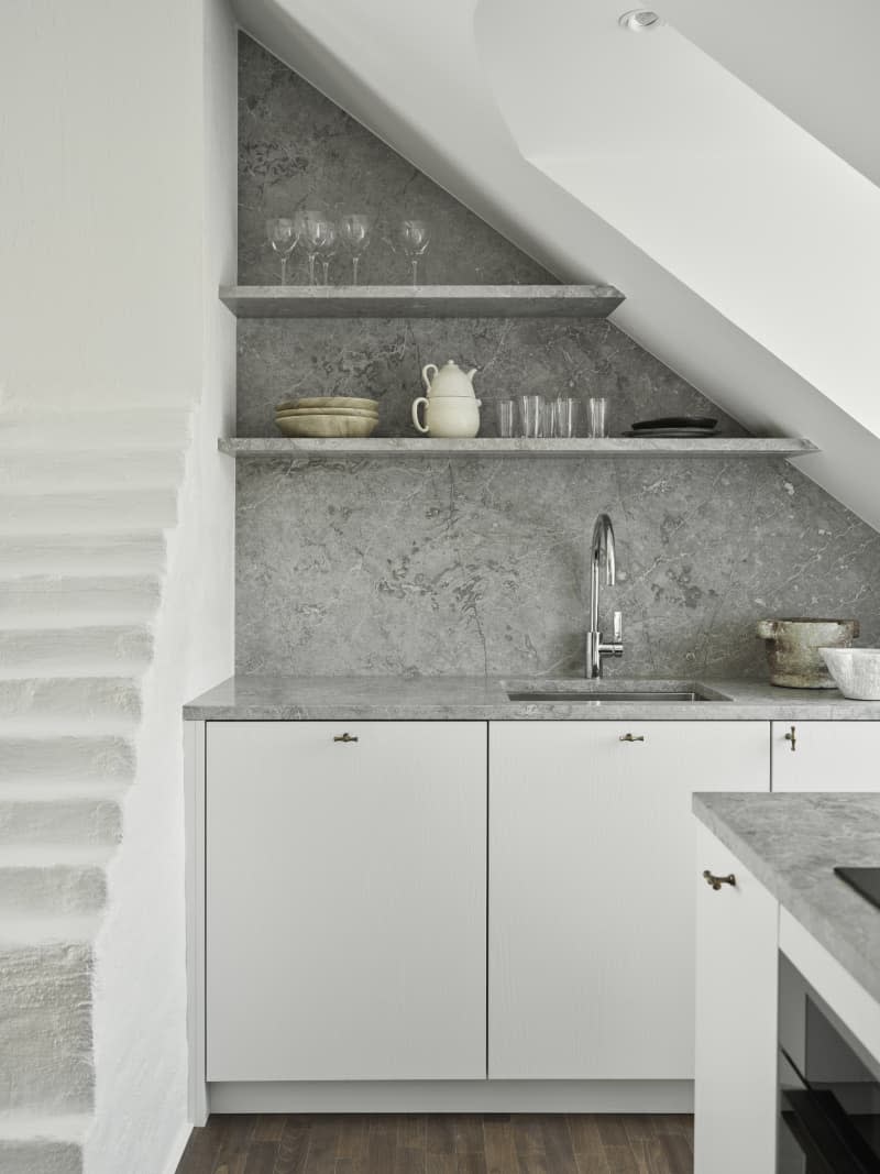 angled ceiling with cut out for window, white cabinets and exposed brick stairs and open shelving