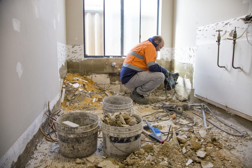 A tradesman squats in a laundry that is undergoing renovation. (Source: Getty)