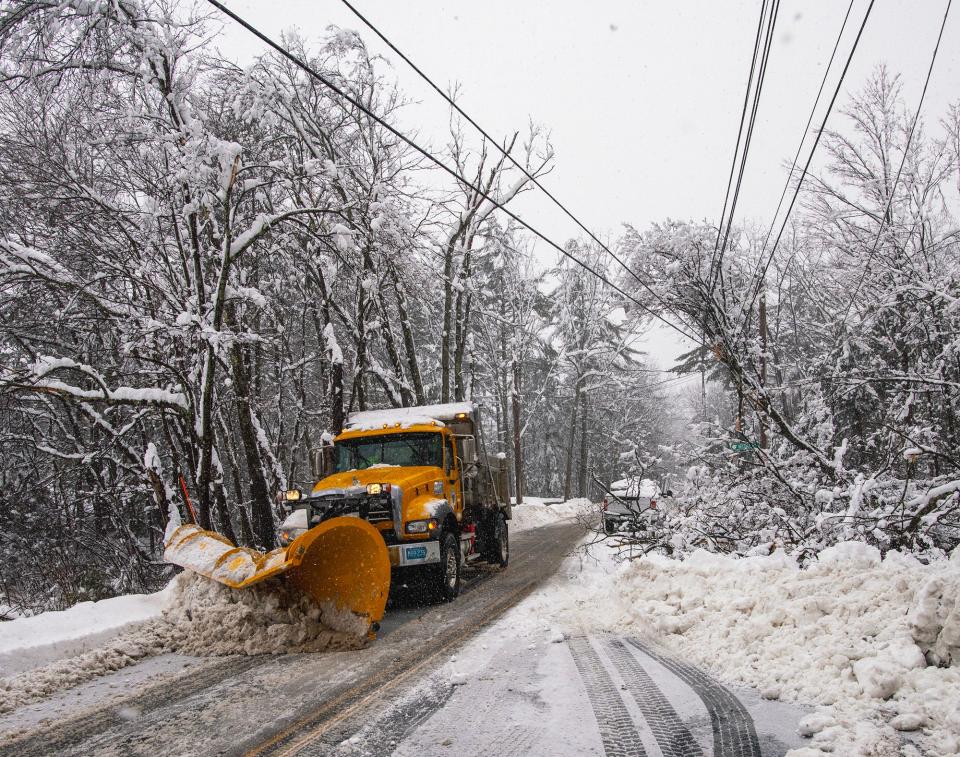 A plow truck clearing a town road passes a tree leaning on power lines in March.