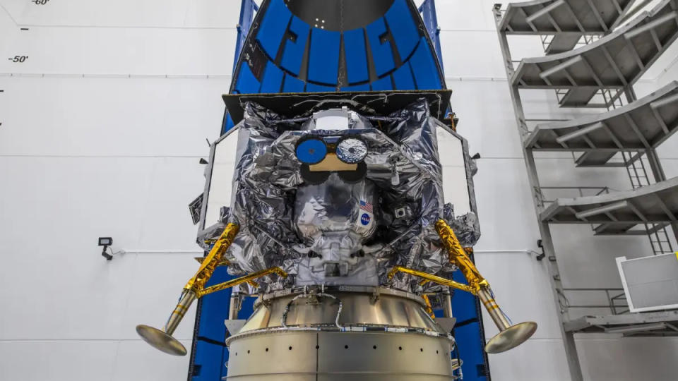 a space lander with protruding legs sits attached to its payload adapter in a white room.  The Peregrine lunar lander, built by Pittsburgh-based company Astrobotic, will launch toward the moon on Jan. 8 atop a United Launch Alliance Vulcan Centaur rocket.