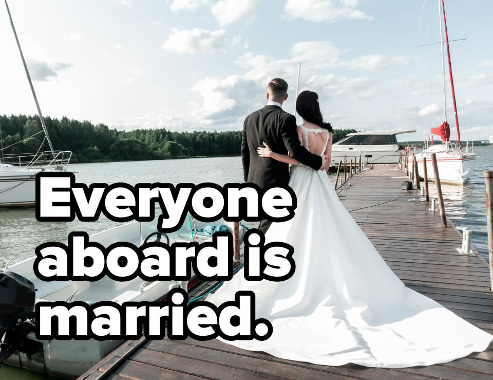 A couple, back facing the camera, stands on a dock next to a boat. The woman is wearing a long wedding dress and the man a black suit