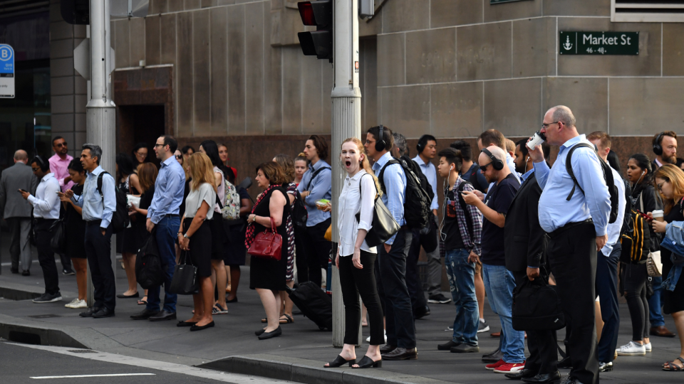 An image of office workers waiting to cross the street in the Sydney CBD as they head to their jobs.