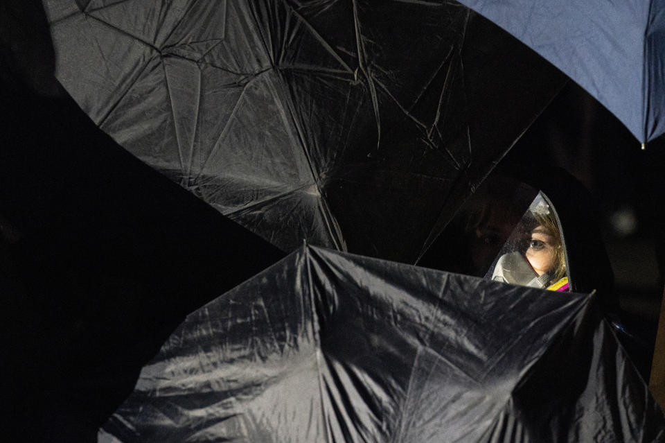 A demonstrator hides behind a phalanx of umbrellas before advancing on a perimeter security fence to agitate authorities during a protest decrying the shooting death of Daunte Wright outside the Brooklyn Center Police Department, Wednesday, April 14, 2021, in Brooklyn Center, Minn. (AP Photo/John Minchillo)