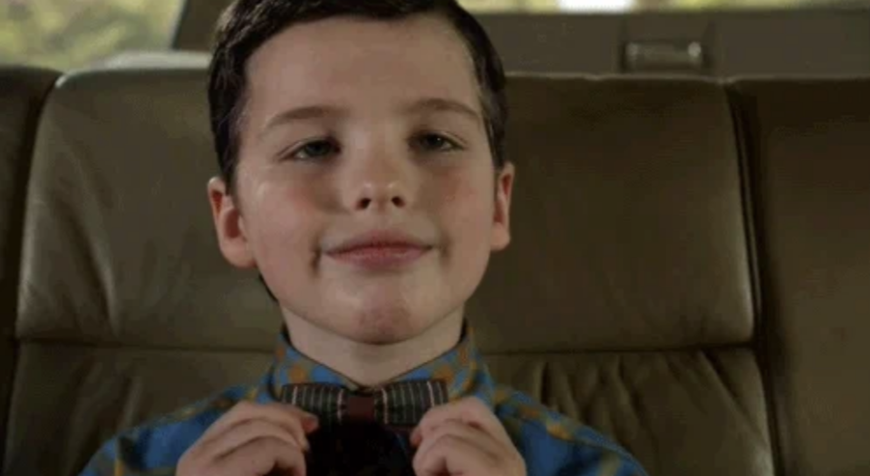 Young Sheldon adjusts his bow tie while sitting in a car