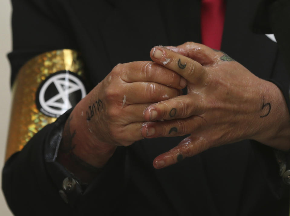 Extinction Rebellion climate protester removes glue from their hands after police removed them after they formed a line and glued themselves to the entrances of the London Stock Exchange in the City of London, Thursday April 25, 2019. (Isabel Infantes/PA via AP)