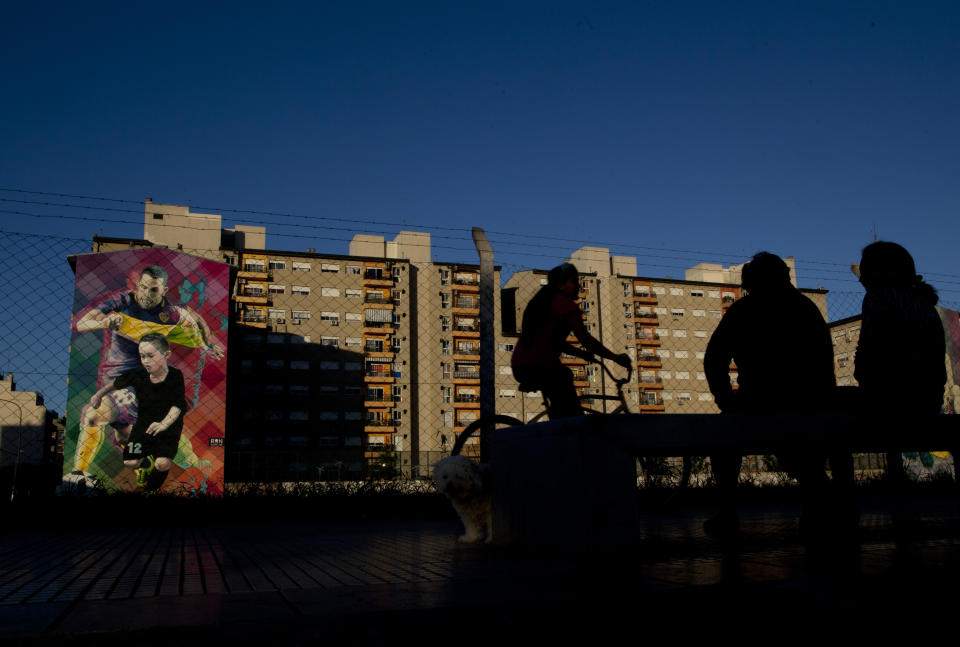 A painting of Boca Juniors player Carlos Tevez is seen on a building as a woman rides a bicycle in Buenos Aires, Argentina Wednesday, Nov. 7, 2018. Boca Juniors will face Play River Plate for the Copa Libertadores final match. (AP Photo/Natacha Pisarenko)