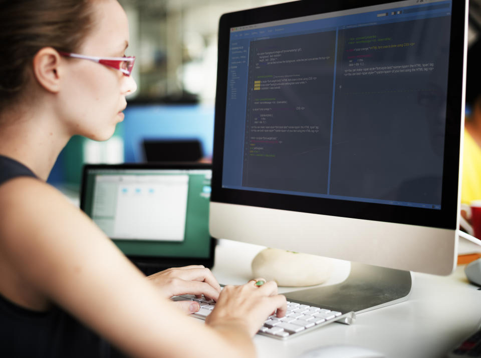 Woman sitting in front of computer screen with code on it.