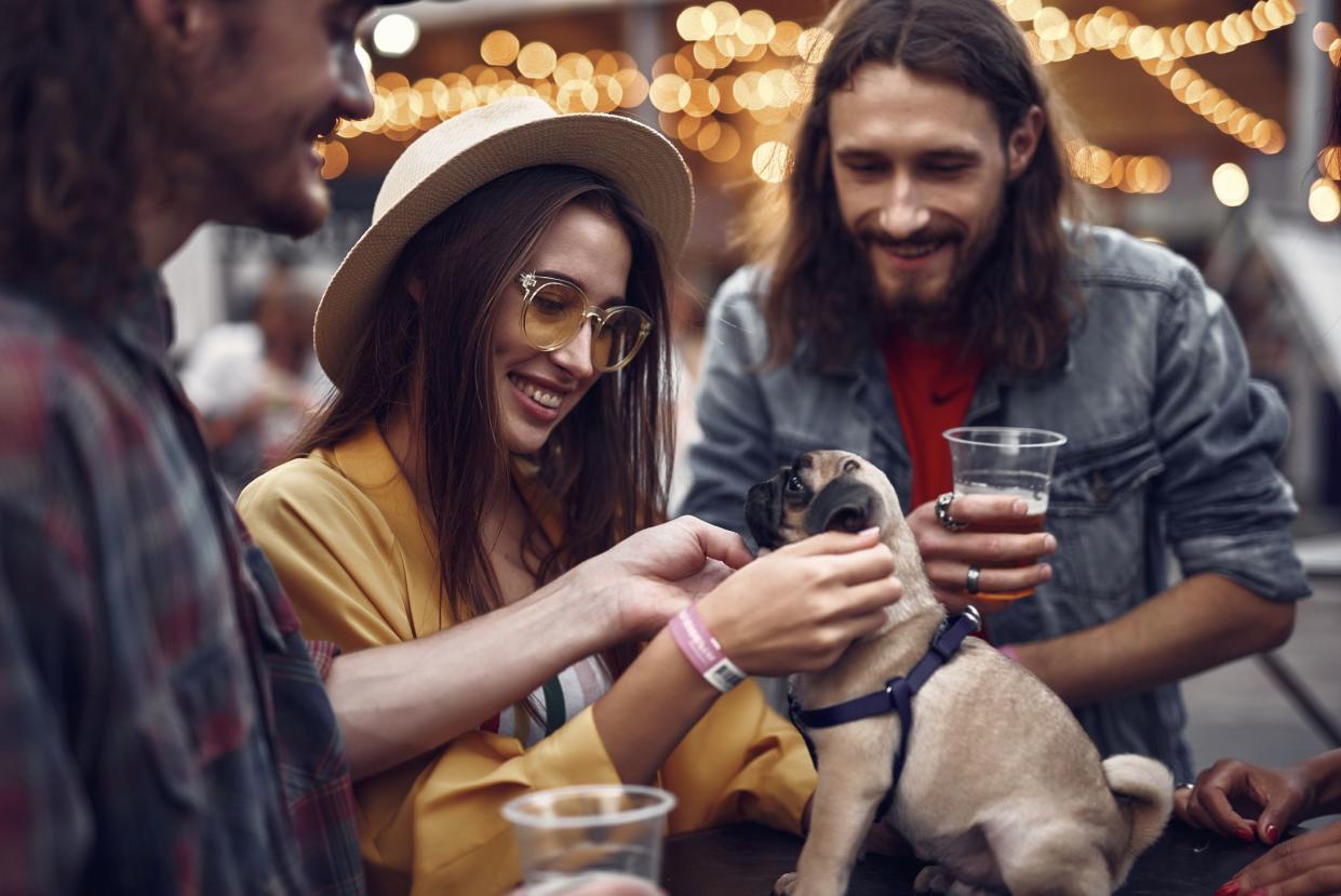 Our four-legged friend. Portrait of stylish hipster friends looking at cute dog and smiling. Bearded guy holding beer