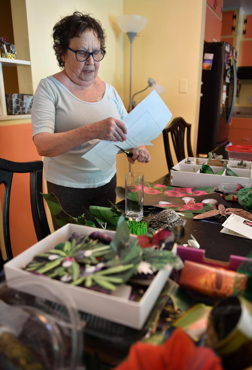 Sandy Payson cuts out a flower a page of a coffee table floral book. Payson has created a garden of sculptural paper flowers in her Sarasota home. 