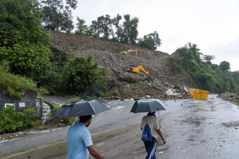 People walk in the rain next to a highway expansion site where heavy rains have disrupted operations and blocked part of the existing road in Dharamshala, India, Monday, Aug. 14, 2023. Heavy monsoon rains triggered floods and landslides in India's Himalayan region, leaving several people dead and many others trapped. (AP Photo/Ashwini Bhatia)