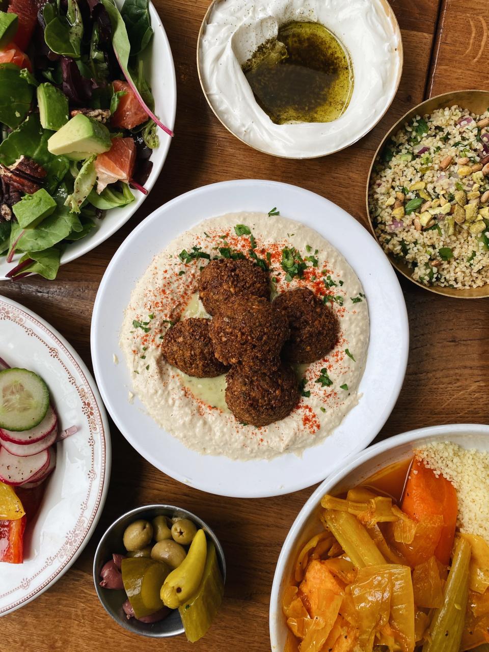 A spread of various Mediterranean food, with a bowl of falafel hummus in the center