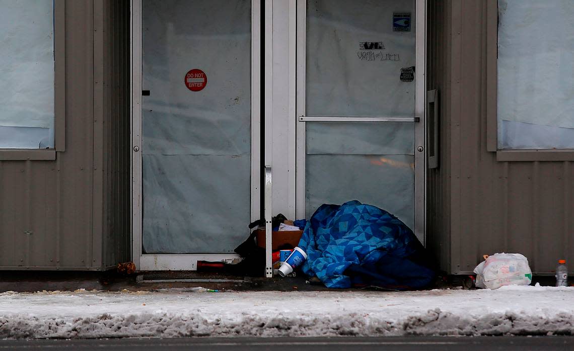 A person sleeps under a blanket with his belongings in the doorway of a closed downtown Kennewick business on a cold and snowy morning. Libraries and other sites will be open as warming sites as temperatures are dip below zero.