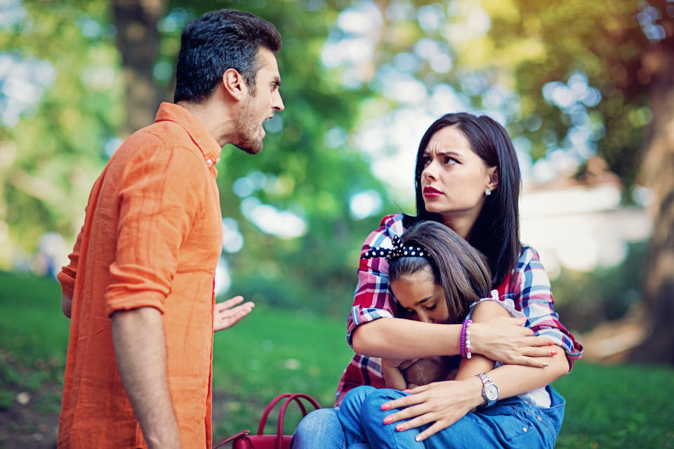 A man and woman having a disagreement while a young girl hugs the woman's leg, outdoors
