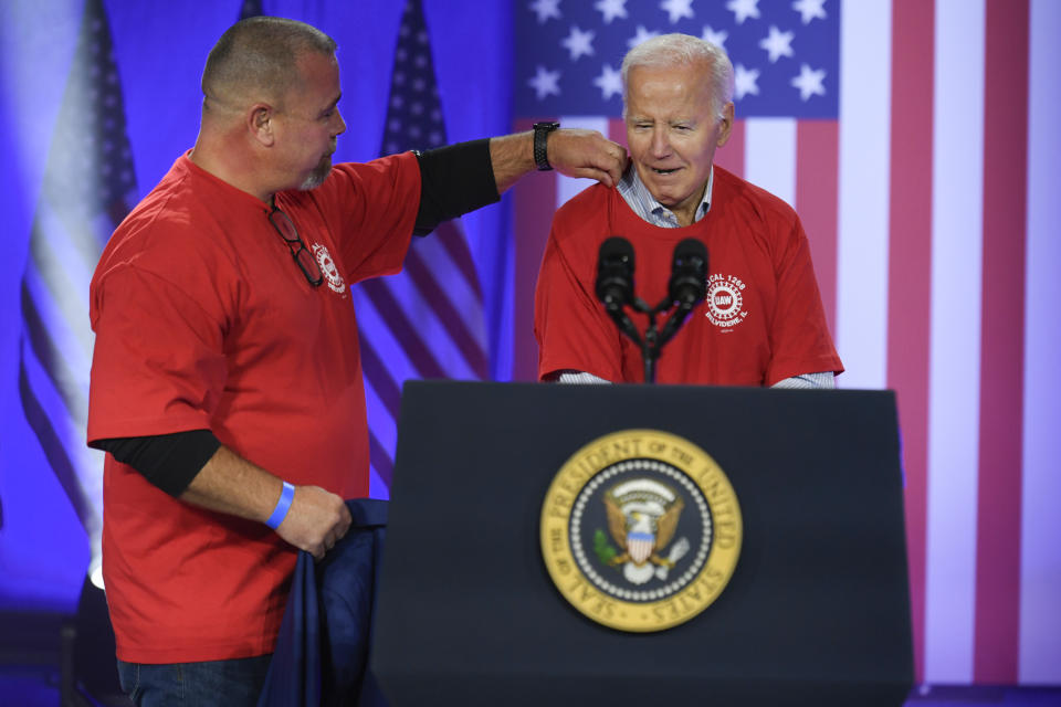 President Joe Biden puts on a UAW Local 1268 shirt with the help of Matt Frantzen, local 1268 president, before he speaks to United Auto Workers at the Community Building Complex of Boone County, Thursday, Nov. 9, 2023, in Belvidere, Ill. (AP Photo/Paul Beaty)