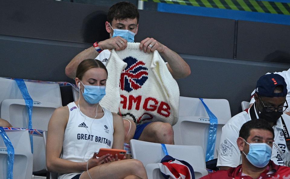 Tom Daley knits a white sweater with the British flag on it in the stands of the Tokyo Olympic Games