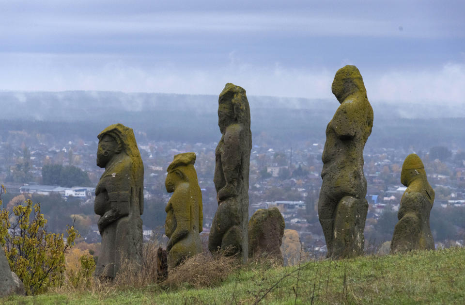 Ancient stone faceless statues of polovets baba (woman), the symbol of ancestors, are seen against the background of recently retaken city of Izium, Kharkiv region, Ukraine, Tuesday, Oct. 25, 2022. The Turkish group of the Polovtsian tribes had inhabited Eastern European steppes in the 11th-13th centuries. There are nine ancient statutes near Izium, one of them was ruined by the Russian shelling. Ukrainian cultural officials have said that 377 cultural objects were damaged or ruined since the Russian invasion on Feb. 24. (AP Photo/Efrem Lukatsky)