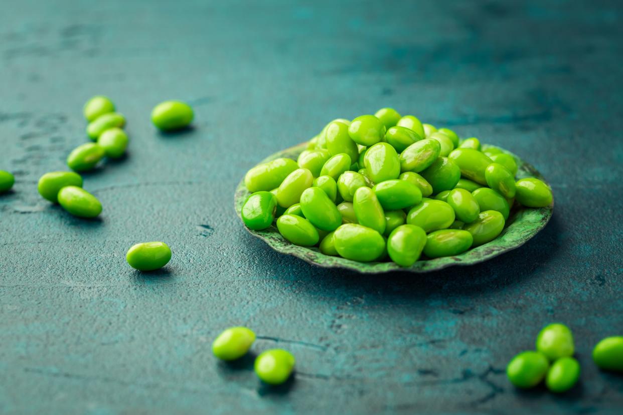 Bowl of raw edamame beans on cyan background