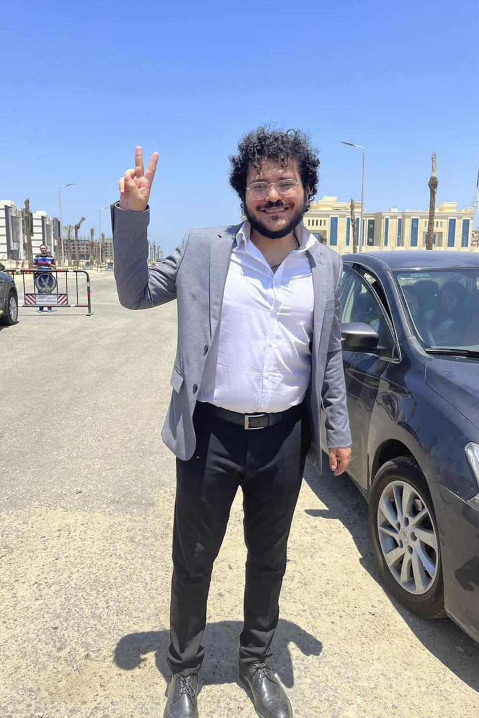 In this photo provided by Patrick Libero page, Patrick George Zaki, a prominent Egyptian rights activist with ties to Italy, flashes "V" sign, Thursday, July 20, 2023, outside the Dakahlia security headquarters in the Nile Delta city of Mansoura, 110 kilometers (70 miles) north of Cairo, Egypt, after he was pardoned by Egyptian President Abdel Fattah el-Sissi along with five other people, according to the country's Official Gazette. Patrick was released from jail Thursday, days after he was sentenced to three years' imprisonment, according to his family and a rights defender. (Patrick Libero page via AP)