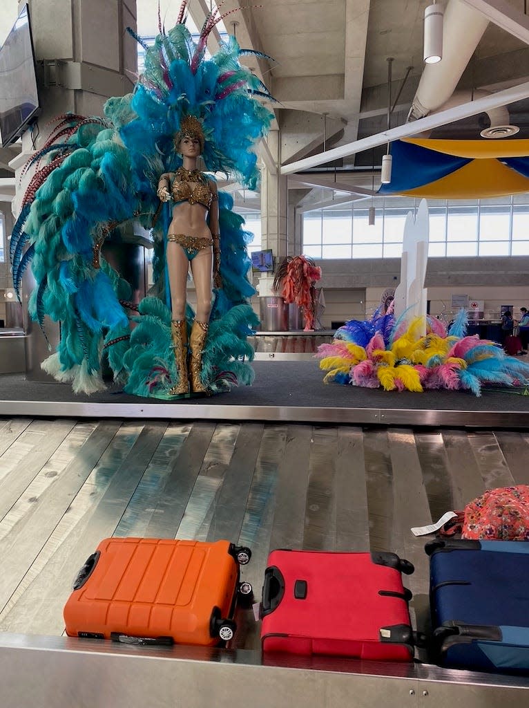 Luggage arriving on an airport belt with a mannequin decked out in feathers for Carnevale.