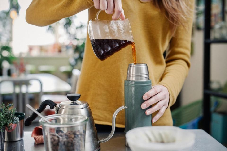 A woman empties a carafe of pour-over coffee into a thermos