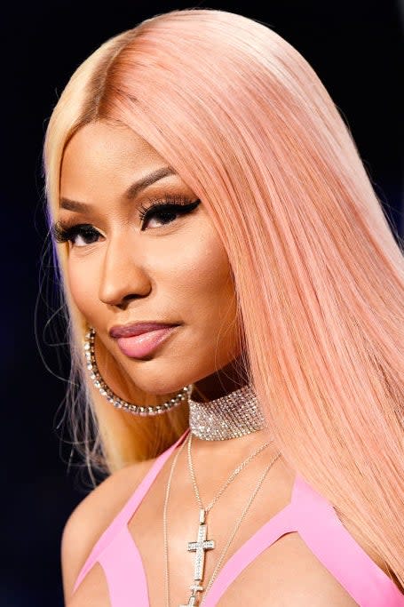 Nicki Minaj poses on the red carpet in a pink dress with long hair and statement jewelry