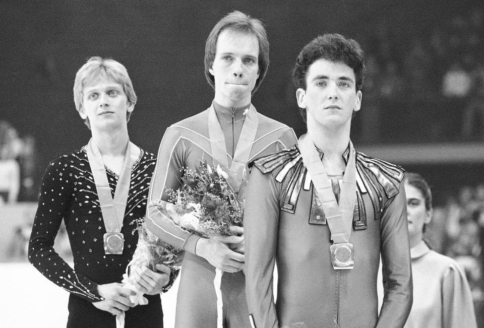 FILE - Scott Hamilton, center, has tears in his eyes as he is flanked by Josef Sabovtchik, left, of Czechoslovakia, and Canada's Brian Orser on the podium after they were awarded gold, bronze and silver medals respectively in the men's free skating competition in Sarajevo, Feb. 16, 1984. Scott Hamilton can scarcely believe that it has been four decades since he stood atop the Olympic podium in Sarajevo. To commemorate the anniversary of that night at Zetra Olympic Hall, the American figure skating icon is planning to reunite with the rest of the podium for a series of events to raise funds for his foundation and the Memorial Sloan Kettering Cancer Center. (AP Photo/File)