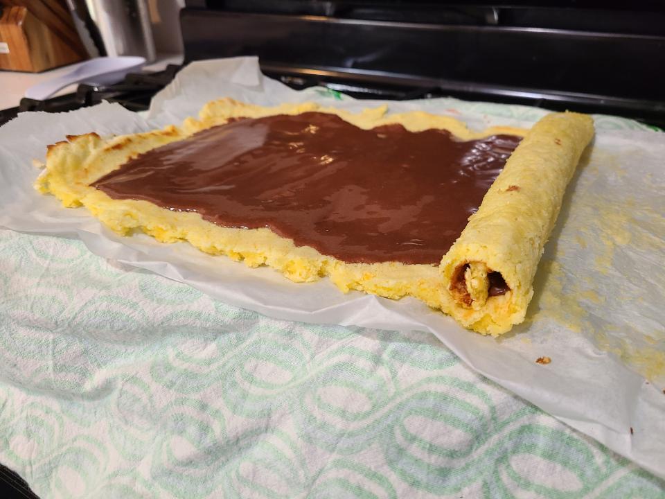 A chocolate frosting inside an orange cake being rolled into a log shape.