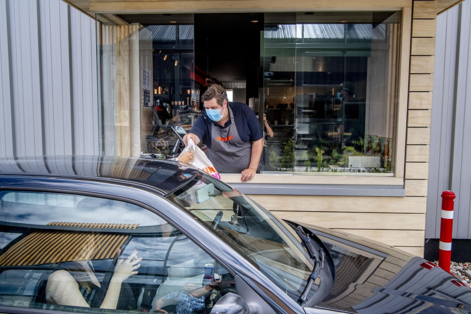 GOES, NETHERLANDS - 2020/07/27: A worker at New York Pizza wearing a mask serves customers through their car at the Pizza drive-thru.
New York Pizza opens the first Pizza Drive-Thru in the Netherlands working together with Dunkin' Donuts, pizza slices and donuts are served through customers' cars. In honor of this opening, a new product was jointly developed; the PizzaDonut available with two different toppings: as Margherita or as Pepperoni. (Photo by Robin Utrecht/SOPA Images/LightRocket via Getty Images)