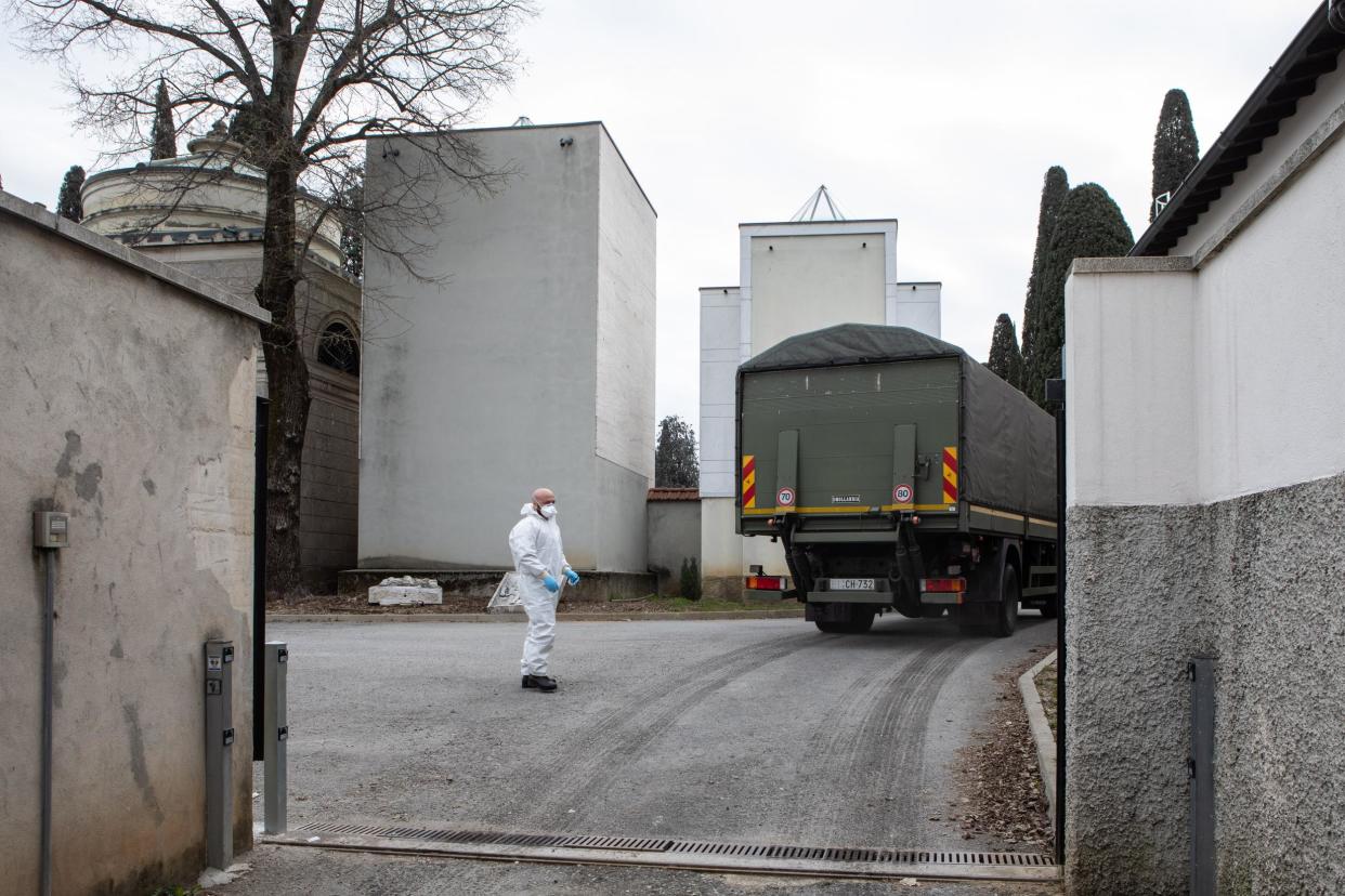 An Italian army officer wearing a protective suit stands as a military vehicle drives in the Monumental Cemetery on March 26 in Bergamo: Emanuele Cremaschi / Getty Images