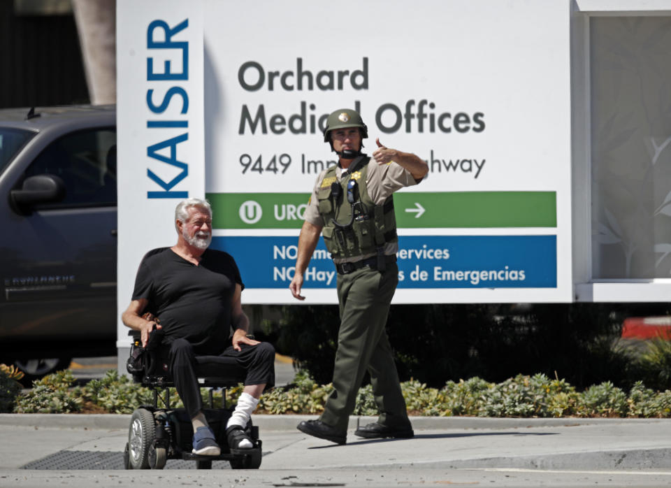 A man in a motorized wheelchair and a Los Angeles County Sheriff's deputy wait outside after staff and patients were evacuated from Kaiser Permanente Downey Medical Center, following reports of someone with a weapon at the facility in Downey, Calif., Tuesday, Sept. 11, 2018. Los Angeles County sheriff's officials say a suspect is in custody and deputies and police officers are methodically searching the complex. (AP Photo/Jae C. Hong)