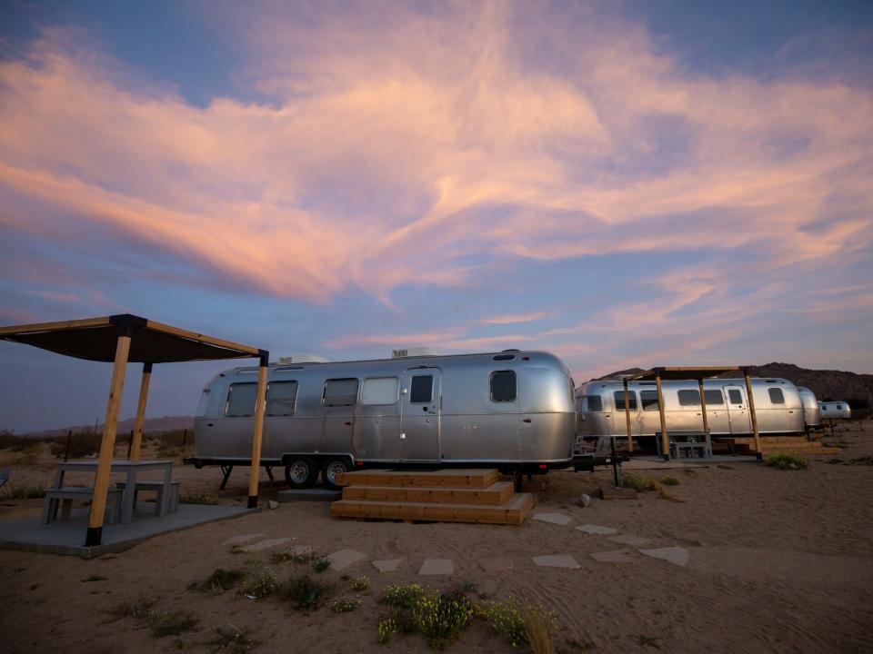 Airstream trailers outside at Autocamp's Joshua Tree location at sunset. There's tables and chairs between each trailer.