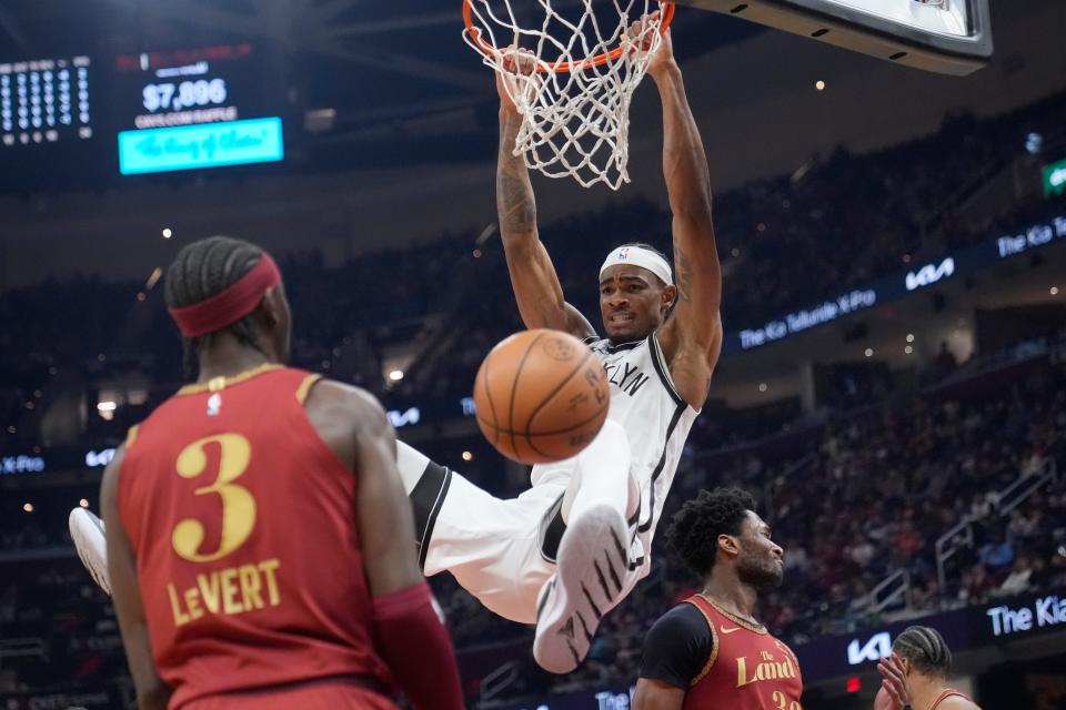 Brooklyn Nets center Nic Claxton (33) hangs from the basket after dunking between Cleveland Cavaliers guard Caris LeVert (3) and center Damian Jones, right, in the first half of an NBA basketball game, Sunday, March 10, 2024, in Cleveland. (AP Photo/Sue Ogrocki)