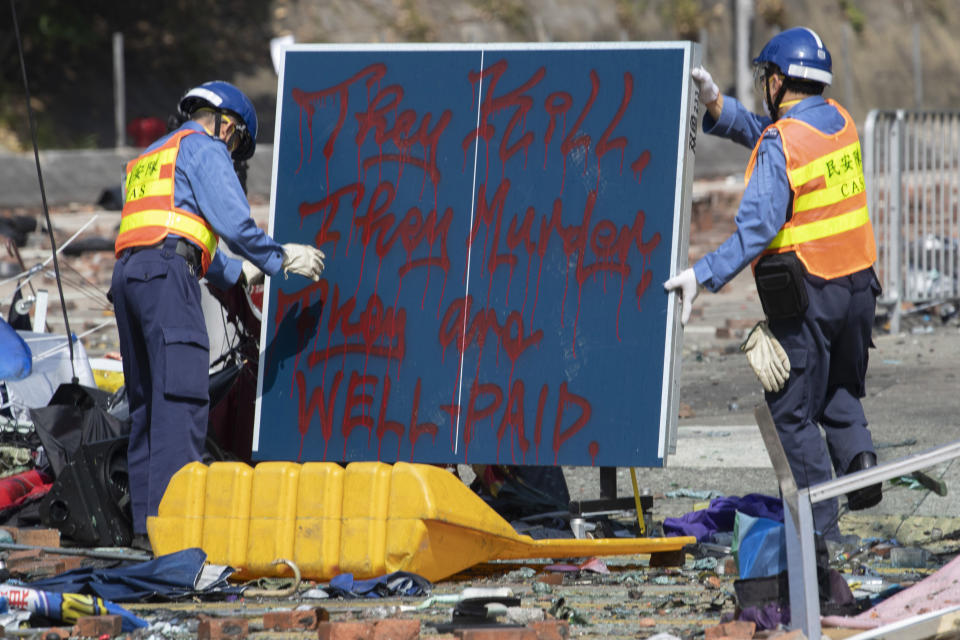 Workers remove a board with the words referring to the police force "They Kill, They Murder, They are well-paid" as they start to clean up the road outside the Hong Kong Polytechnic University in Hong Kong on Wednesday, Nov. 20, 2019. Hong Kong schools have reopened after a six-day shutdown but students were facing transit disruptions as the last protesters remained holed up on a university campus. (AP Photo/Ng Han Guan)