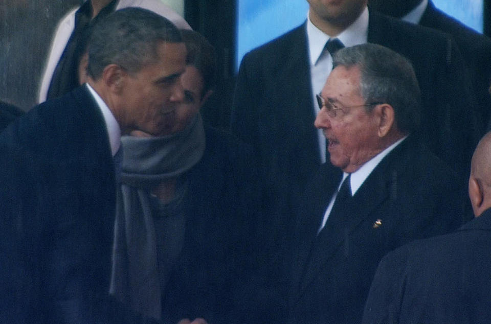 In this image from TV, U.S. President Barack Obama shakes hands with Cuban President Raul Castro at the FNB Stadium in Soweto, South Africa, in the rain for a memorial service for former South African President Nelson Mandela, Tuesday Dec. 10, 2013.