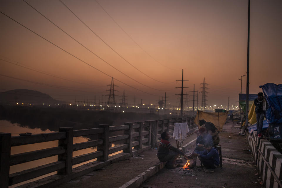 Farmers sit next to a small bonfire at sunset at a protest site against new farm laws at the Delhi-Uttar Pradesh state border, India, Wednesday, Jan. 20, 2021. Farmers have been blockading highways connecting New Delhi to northern India for nearly seven weeks against new farm laws, obstructing transportation and dealing a blow to manufacturing and businesses in the north. Farmers fear the government will stop buying grain at minimum guaranteed prices and that corporations will then push prices down under the new laws. (AP Photo/Altaf Qadri)