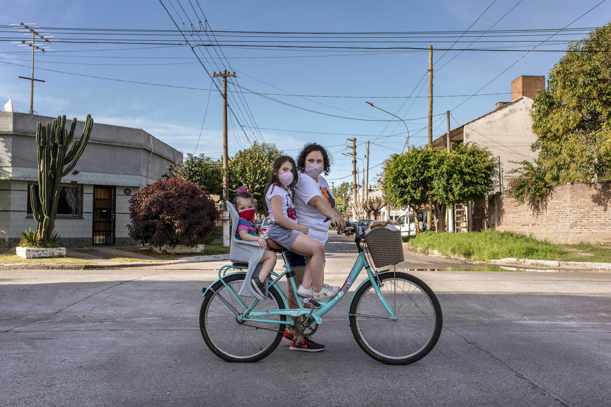 María Teresa Arzamendia stands for a portrait with her two daughters Leia and Catalina and her bicycle with pastries in El Palomar, Buenos Aires Province, on April 17.