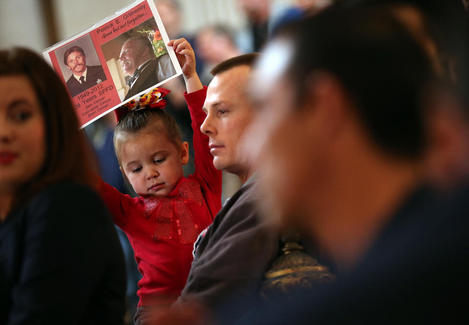 SAN FRANCISCO, CA - MARCH 26:  Kamryn Grimesey holds a photo of her grandfather, Patrick Grimesey, a San Francisco firefighters who died of cancer,  during a remembrance ceremony held for San Francisco firefighters who have died of cancer on March 26, 2014 at San Francisco City Hall in San Francisco, California. Over two hundred pairs of boots were displayed on the steps inside San Francisco City Hall to symbolize the 230 San Francisco firefighters who have died of cancer over the past decade. According to a study published by the National Institute for Occupational Safety and Health, (NIOSH)  findings indicate a direct correlation between exposure to carcinogens like flame retardants and higher rate of cancer among firefighters.  The study showed elevated rates of respiratory, digestive and urinary systems cancer and also revealed that participants in the study had high risk of mesothelioma, a cancer associated with asbestos exposure.  (Photo by Justin Sullivan/Getty Images)