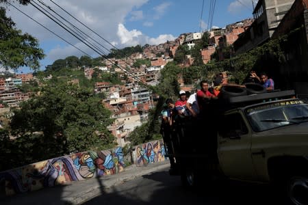 People riding in a truck drive pass by a mural in Petare slum, in Caracas