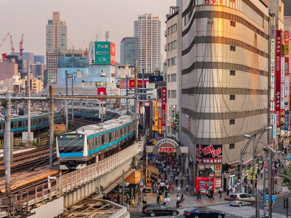 A train travels above a busy street among tall buildings.