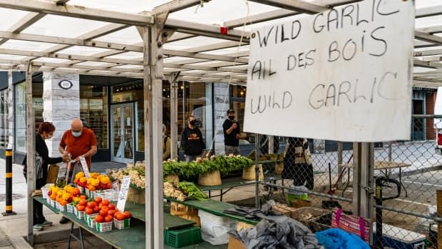 People shop at a distance at a ByWard Market vegetable stall May 10, 2021. The siges advertises garlic and there are also peppers and tomatoes at the stand.