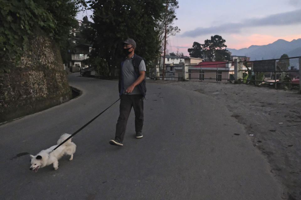 A Naga man wearing a face mask as a precautionary measure against the coronavirus walks his dog in Kohima, capital of the northeastern Indian state of Nagaland, Thursday, Oct. 29, 2020. India's confirmed coronavirus caseload surpassed 8 million on Thursday with daily infections dipping to the lowest level this week, as concerns grew over a major Hindu festival season and winter setting in. (AP Photo/Yirmiyan Arthur)