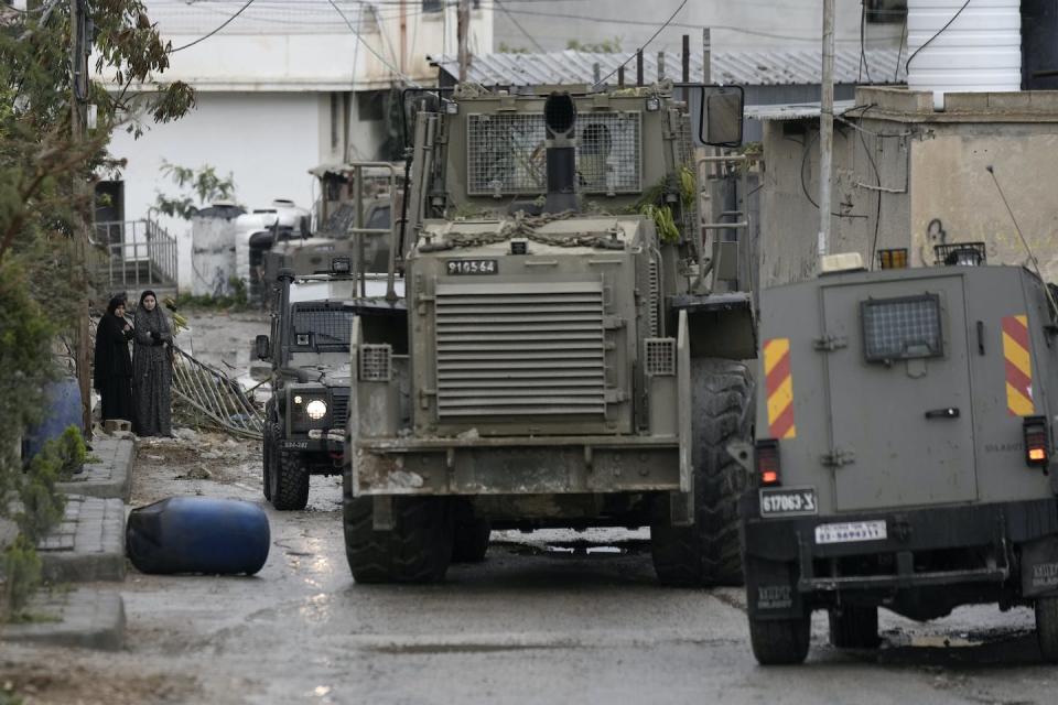 Palestinian women watch Israeli military vehicles, including a bulldozer, in Aqbat Jabr camp, southwest of Jericho on Feb. 4, 2023, during a search for Palestinian suspects after a shooting attack at a restaurant in a nearby settlement. (AP Photo/ Majdi Mohammed)