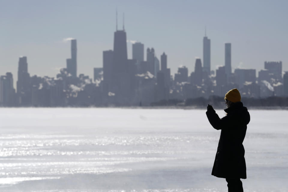 A woman is bundled up as she takes photos of Lake Michigan at Montrose beach in Chicago, Tuesday, Jan. 16, 2024. (AP Photo/Nam Y. Huh)