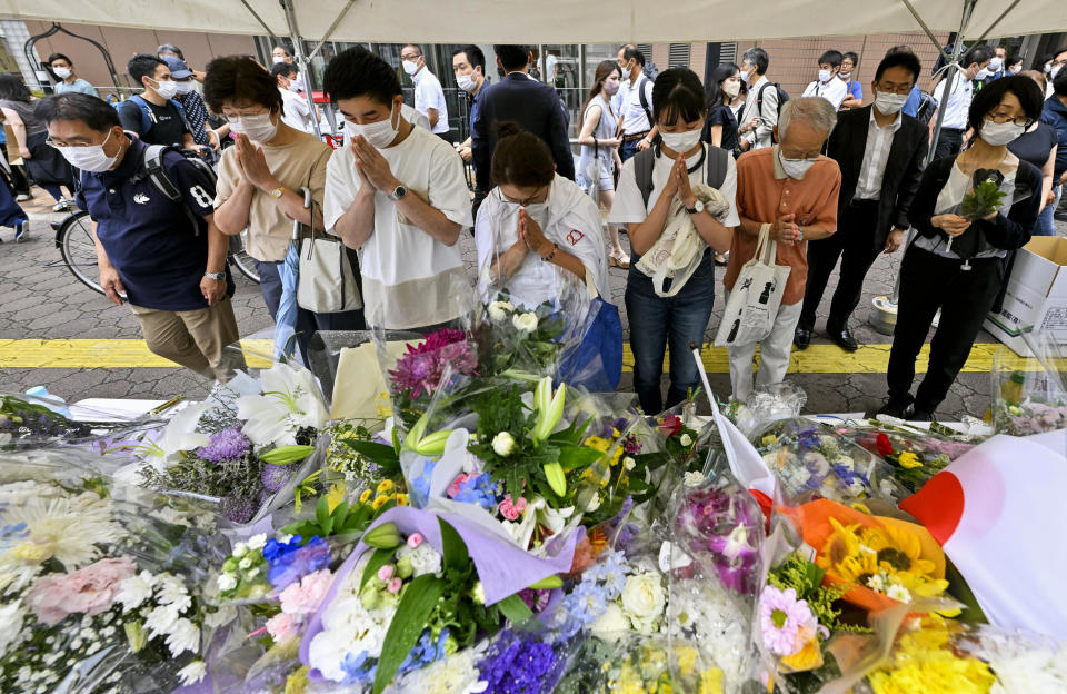 People offer prayers at a makeshift memorial near the scene where the former Prime Minister Shinzo Abe was fatally shot while delivering his speech to support the Liberal Democratic Party's candidate during a Friday's election campaign in Nara, Saturday, July 9, 2022. (Kyodo News via AP)
