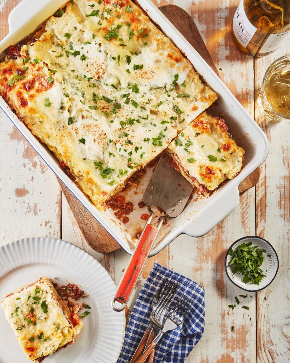 lasagna bolognese in a white rectangle baking dish with a spatula for serving