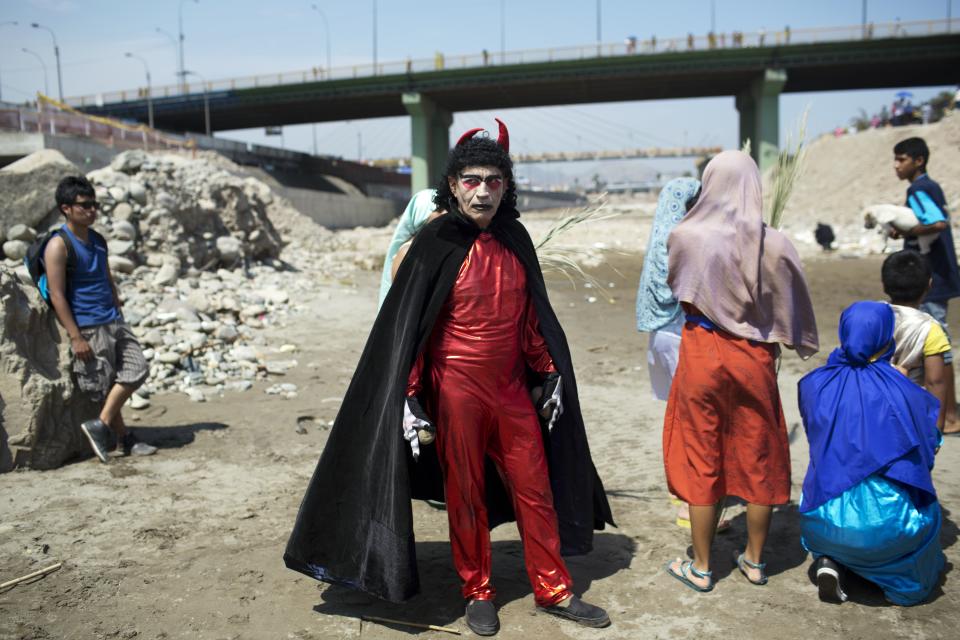 An actor dressed in a devil costume stands on the shores of the Rimac River in Lima, Peru, Thursday, April 17, 2014. The actor performed for people after they attended the reenactment of Jesus' baptism in the river as part of during Holy Week celebrations. (AP Photo/Rodrigo Abd)