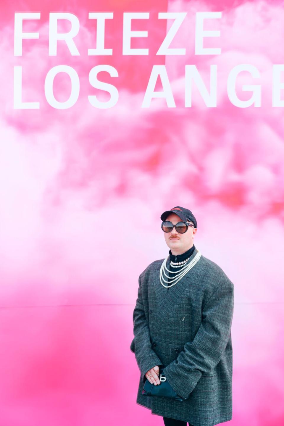 A person posing in front of a pink wall.